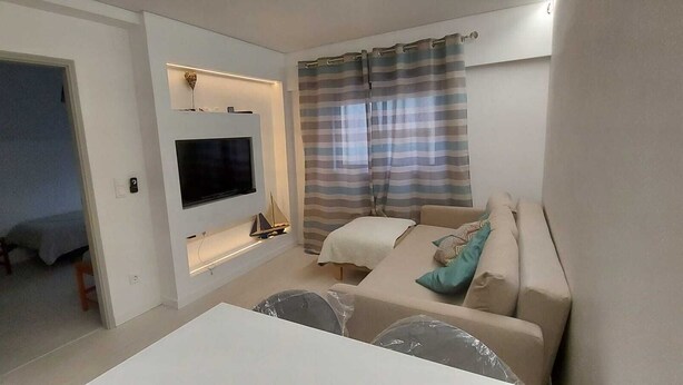 Ein gemütlicher Wohnbereich mit Fernseher, einer Couch, einem kleinen Tisch und einem Fenster mit gestreiftem Vorhang.