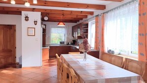 Una cucina con mobili in legno, un tavolo da pranzo con sedie, una finestra con tende e un orologio appeso al muro.