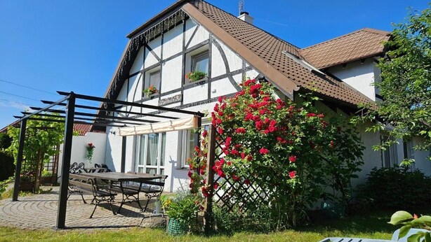 Una casa a due piani con un patio sul giardino, una pergola e una pianta fiorita rossa.