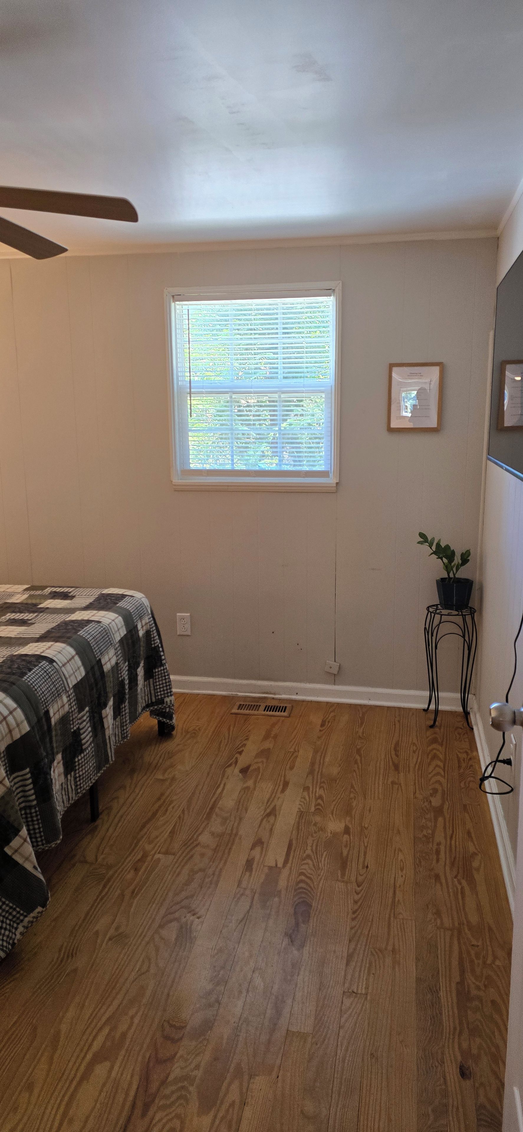 A bedroom with a bed, a window, a radiator, and a small table with a plant.