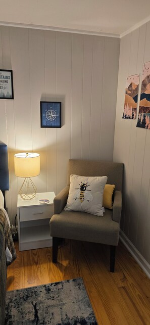 Ett vardagsrum med en grå fåtölj, ett sidobord med en lampa, en inramad kompass och en inramad tavla på väggen.