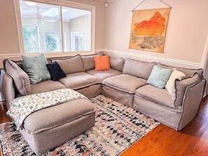 A sectional sofa with an ottoman, a patterned rug, and a wall-mounted artwork.