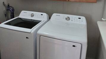 Une buanderie équipée de deux machines à laver et de deux sèche-linge à chargement frontal, tous deux de couleur blanche, avec des armoires en bois au-dessus et un tapis à motifs sur le sol.