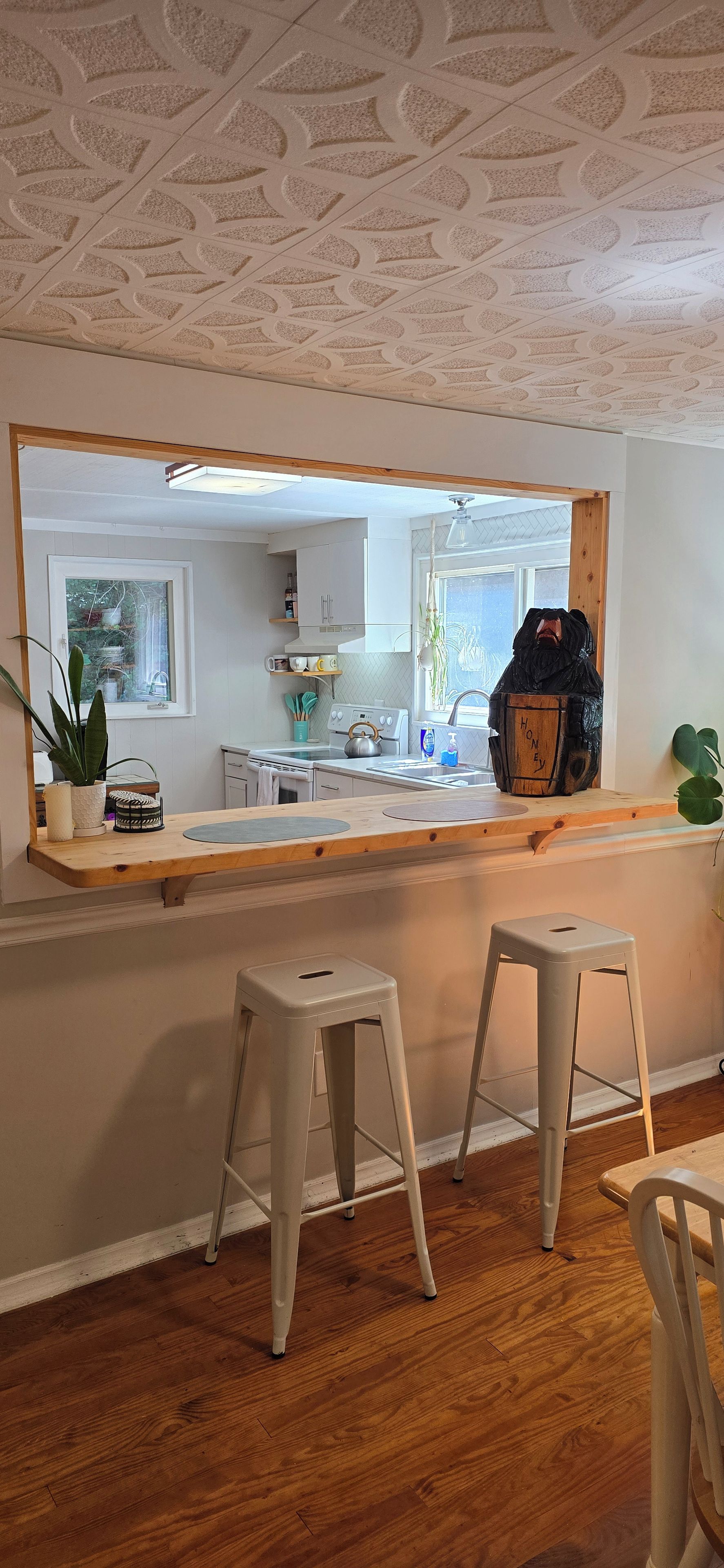 Una cucina con un'ampia finestra, sgabelli di legno e un bancone con diversi oggetti.