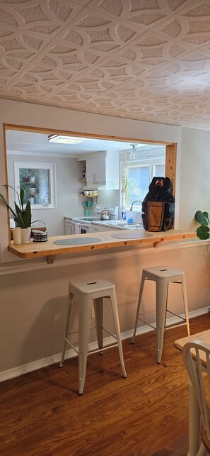 A kitchen with a large window, wooden stools, and a countertop with various items. - Honeybee Haven - Scenic Mountain Getaway - WiFi - Pets OK (Hendersonville)