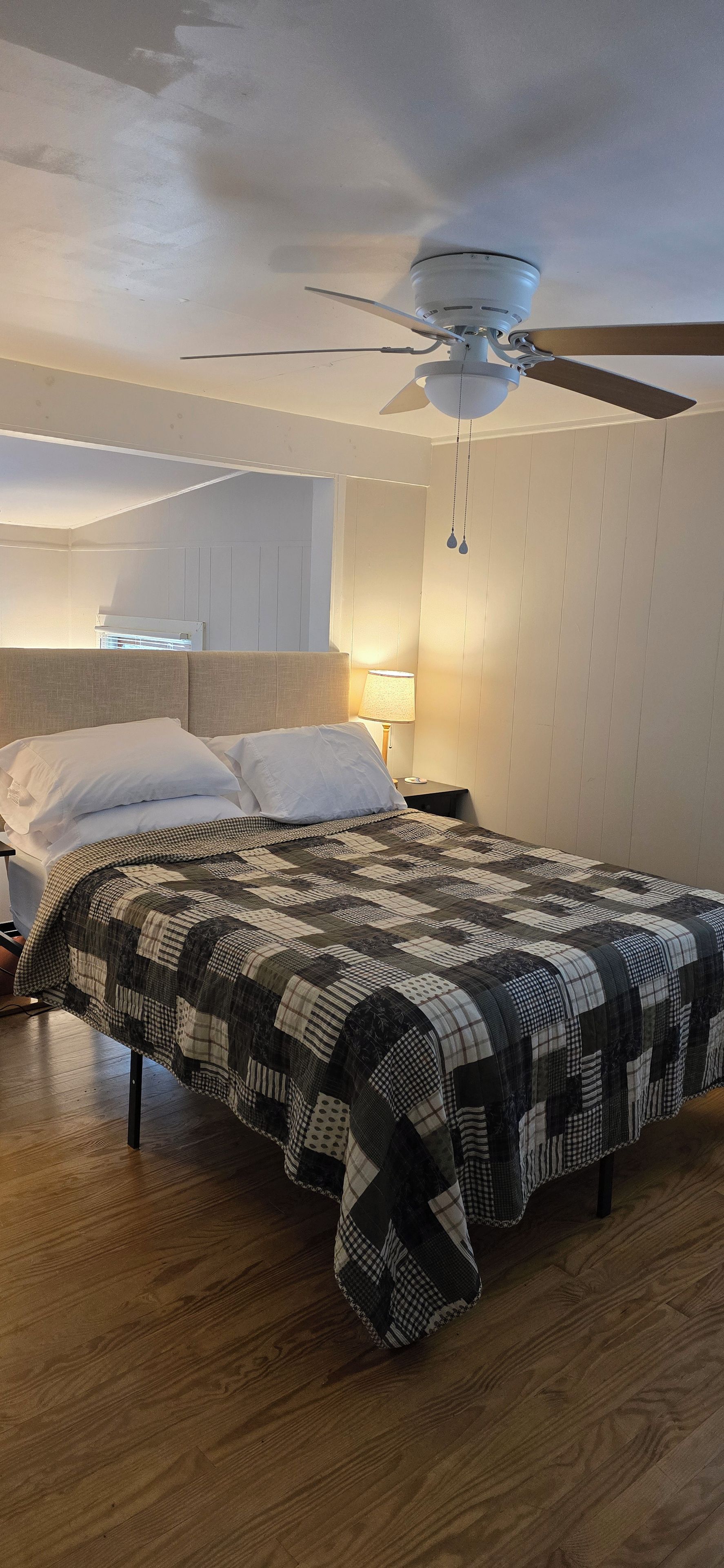 Ein Schlafzimmer mit einem Bett, einem Deckenventilator und einem Nachttisch mit Lampe.