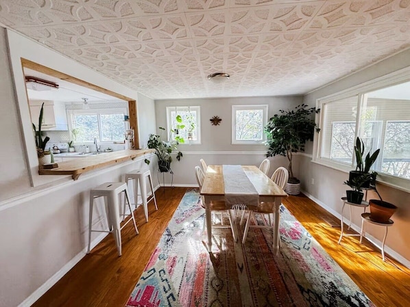 A dining area with a wooden table, white chairs, a patterned rug, and a ceiling with a geometric design.