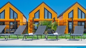 A modern hotel with a pool area, featuring three wooden buildings with large windows and a row of sun loungers. - Premium Holiday home with a pool, sauna, jacuzzi in Kopan (Kopan)