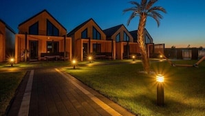 A row of modern wooden buildings with large windows, a paved walkway, and a palm tree. - Premium Holiday home with a pool, sauna, jacuzzi in Kopan (Kopan)