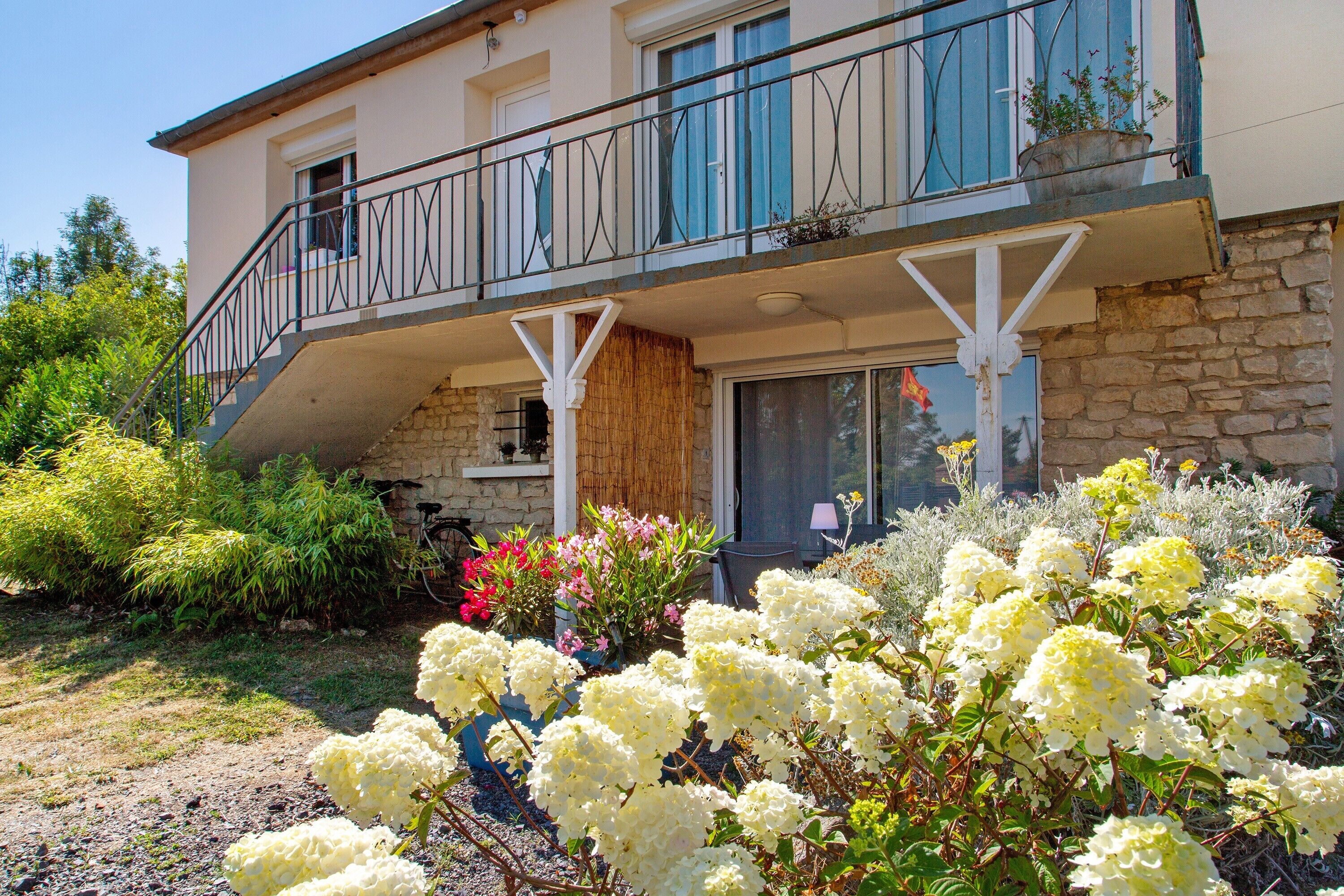 Ein zweistöckiges Gebäude mit Balkon, Steinmauern und einem Garten mit weißen Blumen.