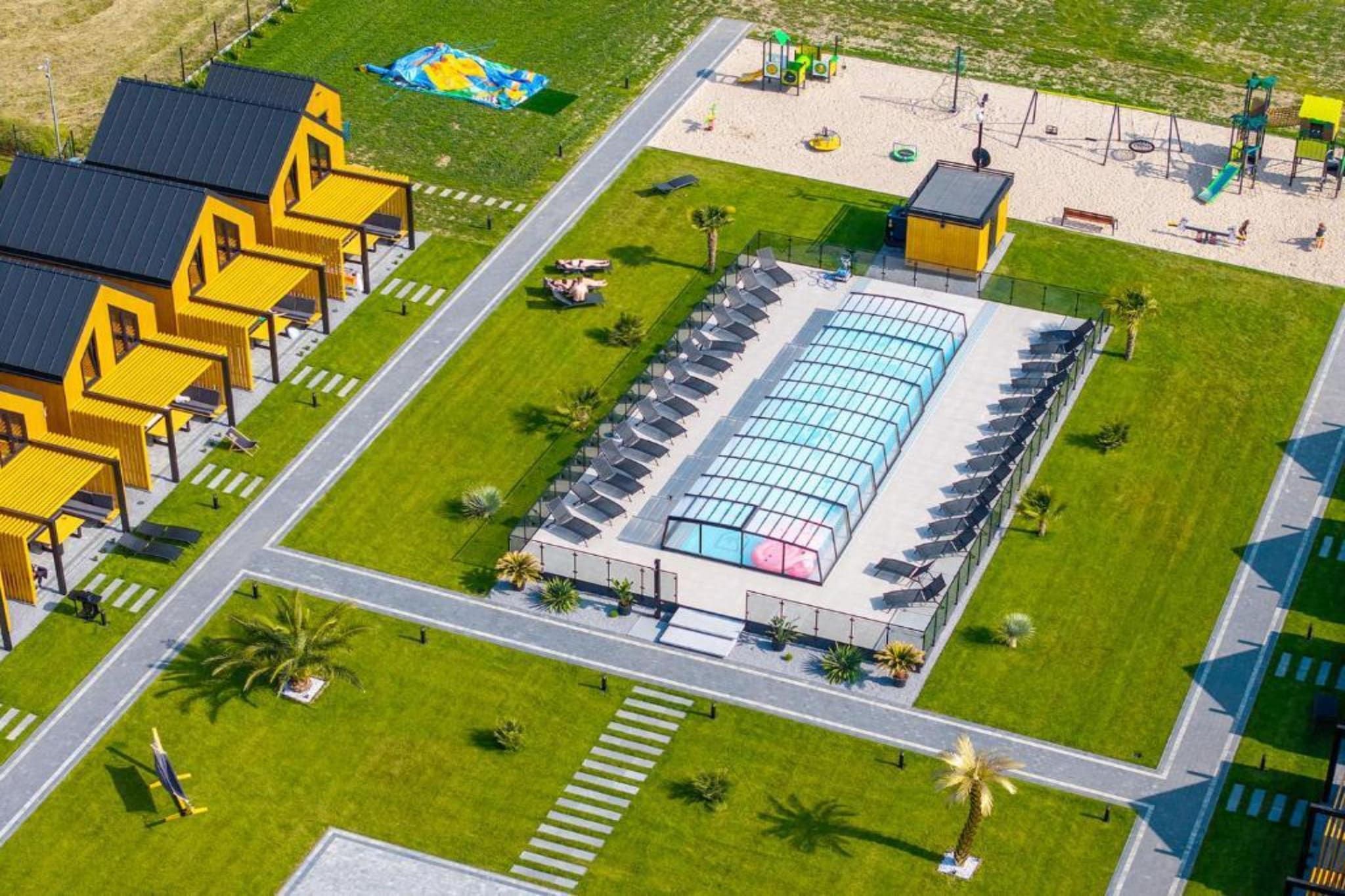 An aerial view of a hotel with a large swimming pool, multiple guest rooms, and a children's play area.
