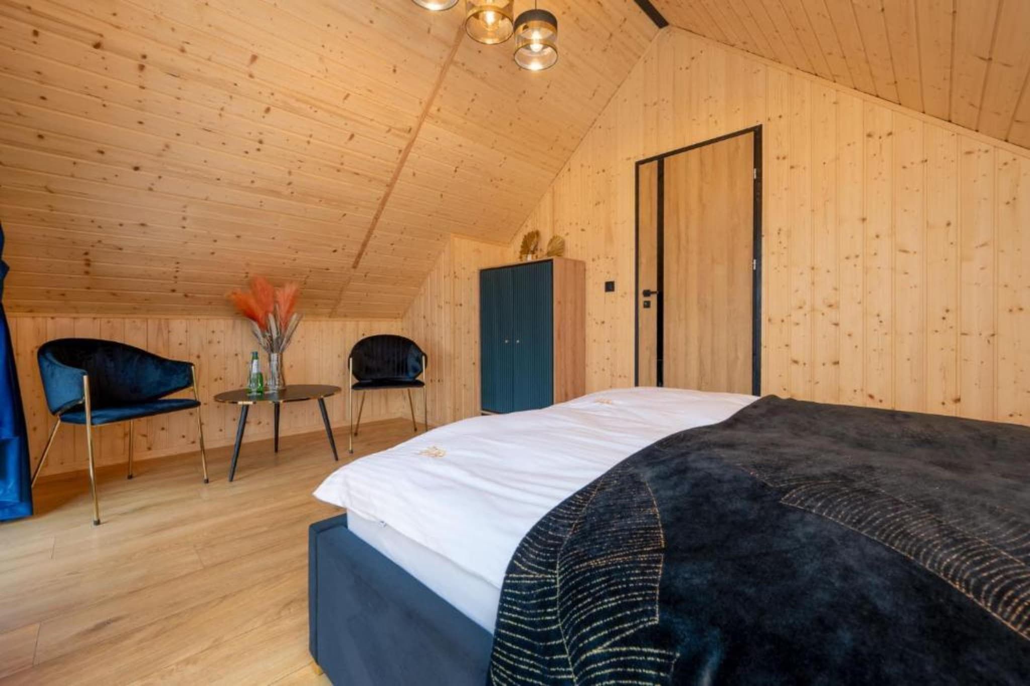 A bedroom with a bed, two chairs, a small table, and a wardrobe.