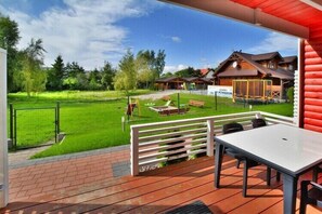 A covered outdoor area with a table and chairs, a grassy lawn, and a wooden building in the background.