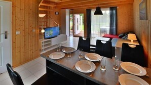 Ein Holzinterieur mit Esstisch, gedeckt für vier Personen, einem Fernseher und Blick ins Freie.