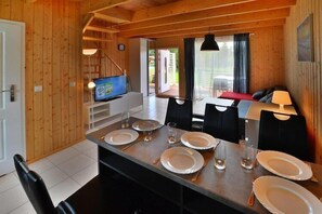 A wooden interior with a dining table set for four, a television, and a view of the outdoors.