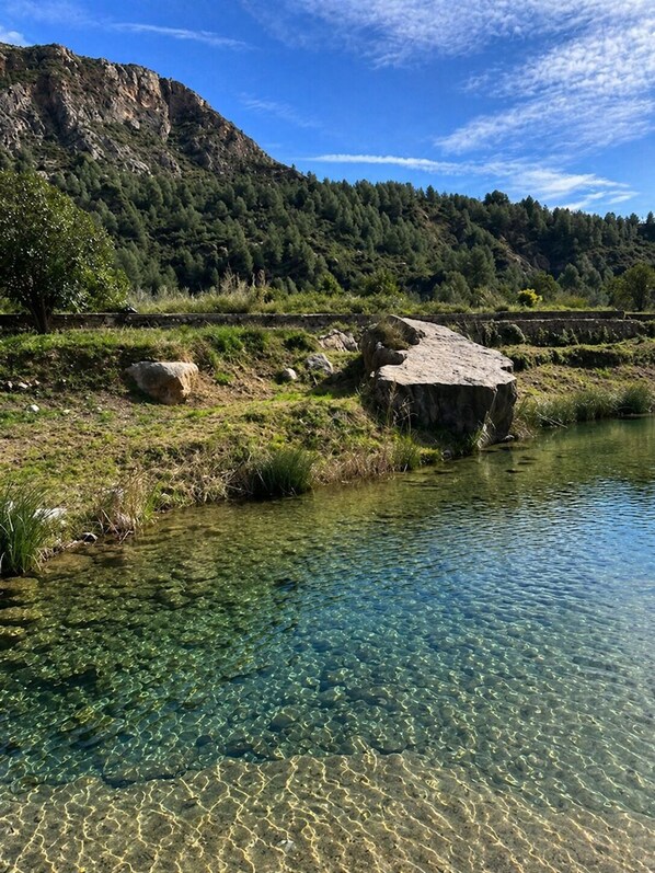 A clear river with visible rocks and a mountainous backdrop.