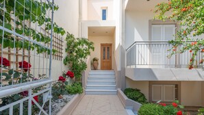 A narrow outdoor corridor with a staircase leading to a door, surrounded by plants and a railing. - Apartment 'Maria Suite 2' with Sea View, Wi-Fi and Air Conditioning (Mirtos)