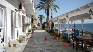 A seaside hotel corridor with stone flooring, potted plants, outdoor seating, and a view of the sea. - Apartment 'Maria Suite 2' with Sea View, Wi-Fi and Air Conditioning (Mirtos)