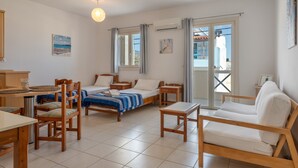 A room with a bed, two bedside tables, a sofa, a dining table with chairs, and a view through a glass door. - Apartment 'Maria Suite 2' with Sea View, Wi-Fi and Air Conditioning (Mirtos)