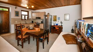 A compact kitchen with wooden cabinets, a dining table with chairs, a refrigerator, and a bookshelf with books. - Villa 'Apartment 2' with Private Terrace (Archanes)