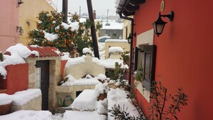 A narrow alley with snow-covered buildings, a tree with oranges, and a red wall with a light fixture. - Villa 'Apartment 2' with Private Terrace (Archanes)