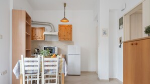 A kitchen with wooden cabinets, a white refrigerator, a table with chairs, and a hanging light fixture. - Apartment 'Deluxe Corner  No 3' with Sea View, Wi-Fi and Air Conditioning (Ierapetra)