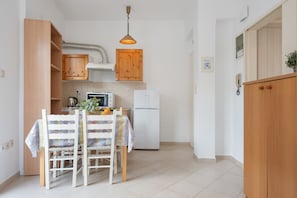 A kitchen with wooden cabinets, a white refrigerator, a table with chairs, and a hanging light fixture.