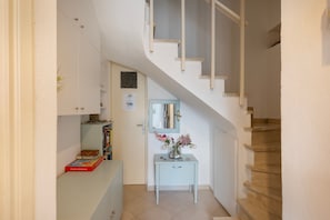 Eine Treppe führt zu einer Empfangsebene mit einer weißen Wand, einer Tür und einem kleinen Tisch mit einem Blumenstrauß.