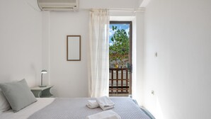 A hotel room with a bed, a nightstand, a lamp, a window with curtains, and a view of the outside. - Apartment 'Deluxe Corner  No 3' with Sea View, Wi-Fi and Air Conditioning (Ierapetra)