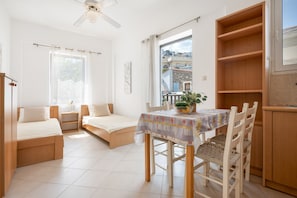 A bedroom with a bed, a small table with a plant, a window, and a balcony.