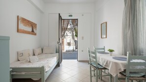 Una habitación con cama, una mesa, sillas, un cuadro y vistas a través de un puerta abierta.