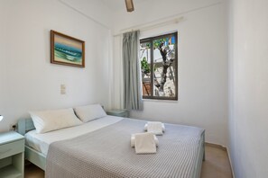 Ein Schlafzimmer mit Bett, Nachttisch, Lampe, einem Fenster mit Vorhängen und einem Bild an der Wand.