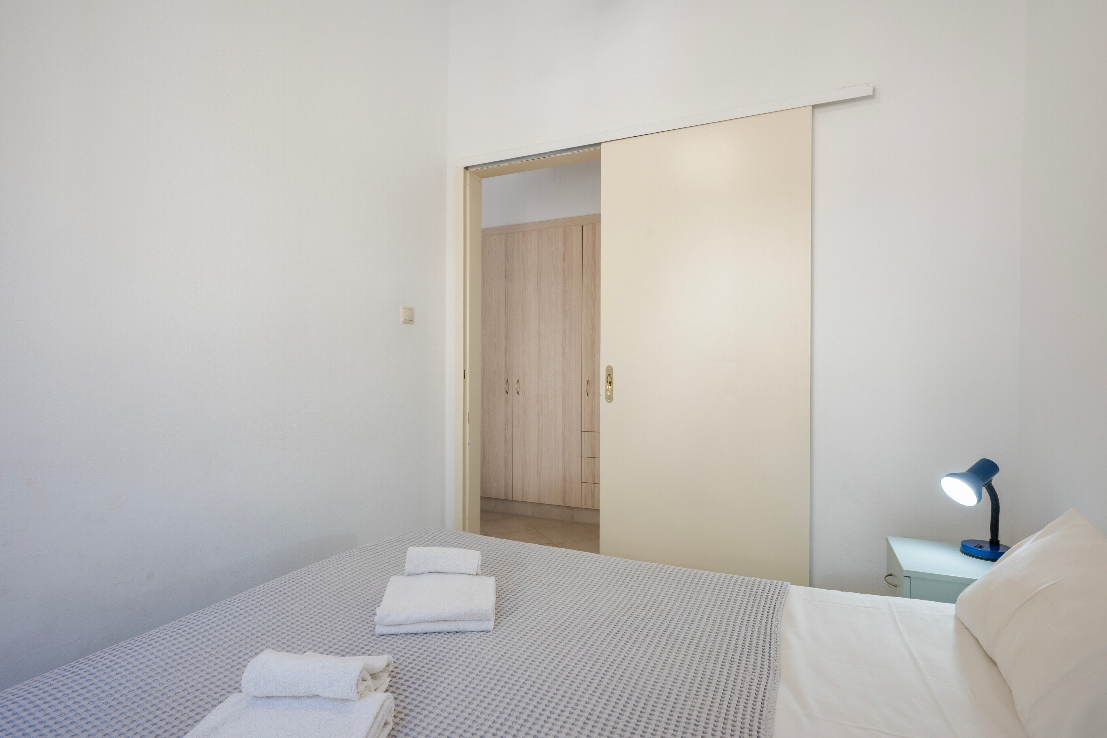 Een slaapkamer met een bed, nachtkastje, bureaulamp en een kledingkast.