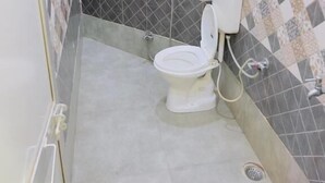 Une salle de bain comprenant des toilettes, une douche et un mur recouvert de carreaux disposés en motif losange.