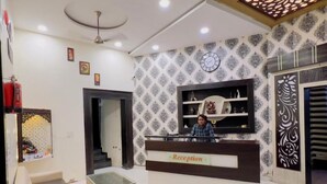 Un comptoir d’accueil avec une horloge, un papier peint à motifs et un canapé dans un espace d’attente.