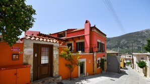 A narrow street with a red building, a small tree, and a mountain in the background.
