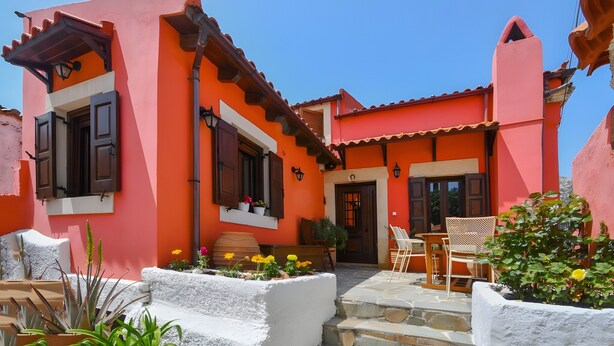 A building with a red facade, a wooden door, and a patio area with outdoor furniture.