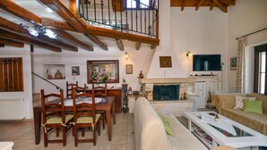 A spacious living room with a fireplace, wooden furniture, and a high ceiling with exposed beams.