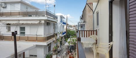 A narrow urban street with buildings, a balcony with a chair, and outdoor seating.
