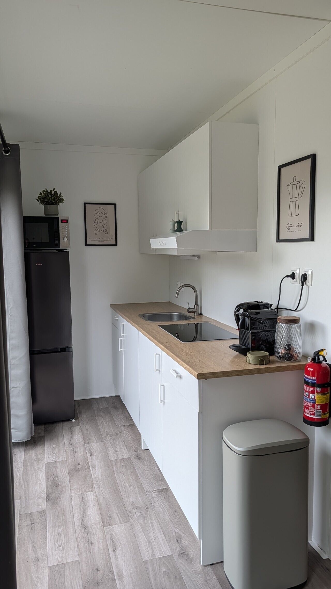 A compact kitchen with a sink, a microwave, a refrigerator, and a coffee machine.