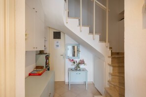 Eine Treppe führt zu einer Empfangsebene mit einer weißen Wand, einer Tür und einem kleinen Tisch mit einem Blumenstrauß.