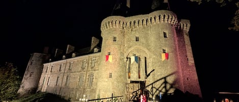 A historic castle with a large central tower, a main entrance, and a bridge leading to the castle.