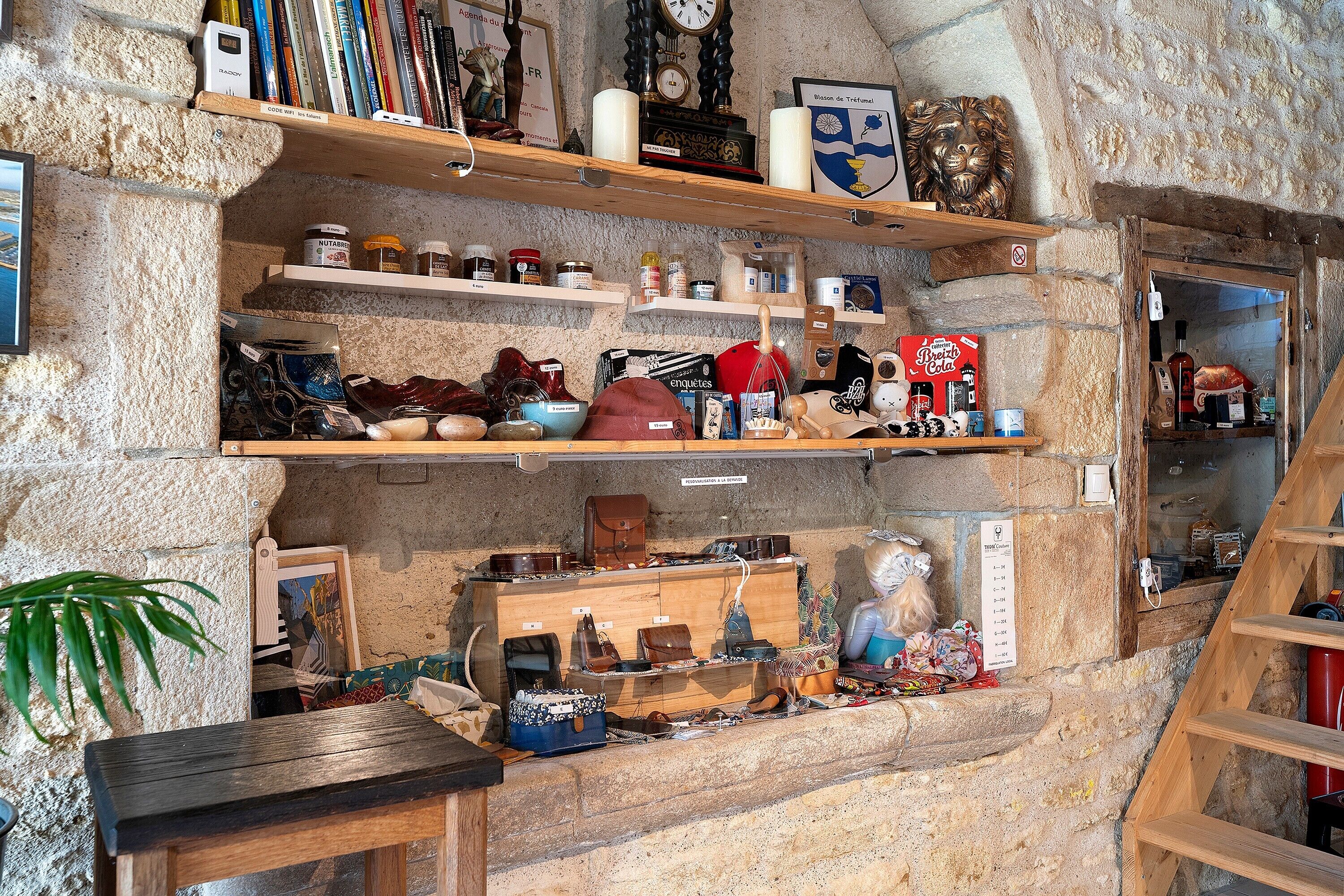 A stone-walled room with shelves displaying books, a clock, and various items.