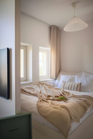 Ein Schlafzimmer mit Bett, Fernseher, Fenster und Deckenleuchte.
