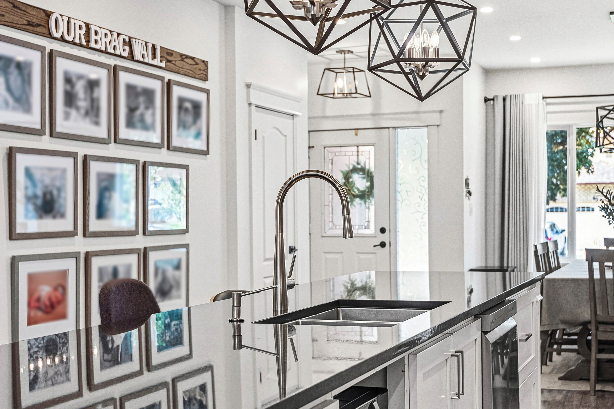 A modern kitchen with a glass backsplash, stainless steel appliances, and a 'OUR BRAG WALL' above the sink.