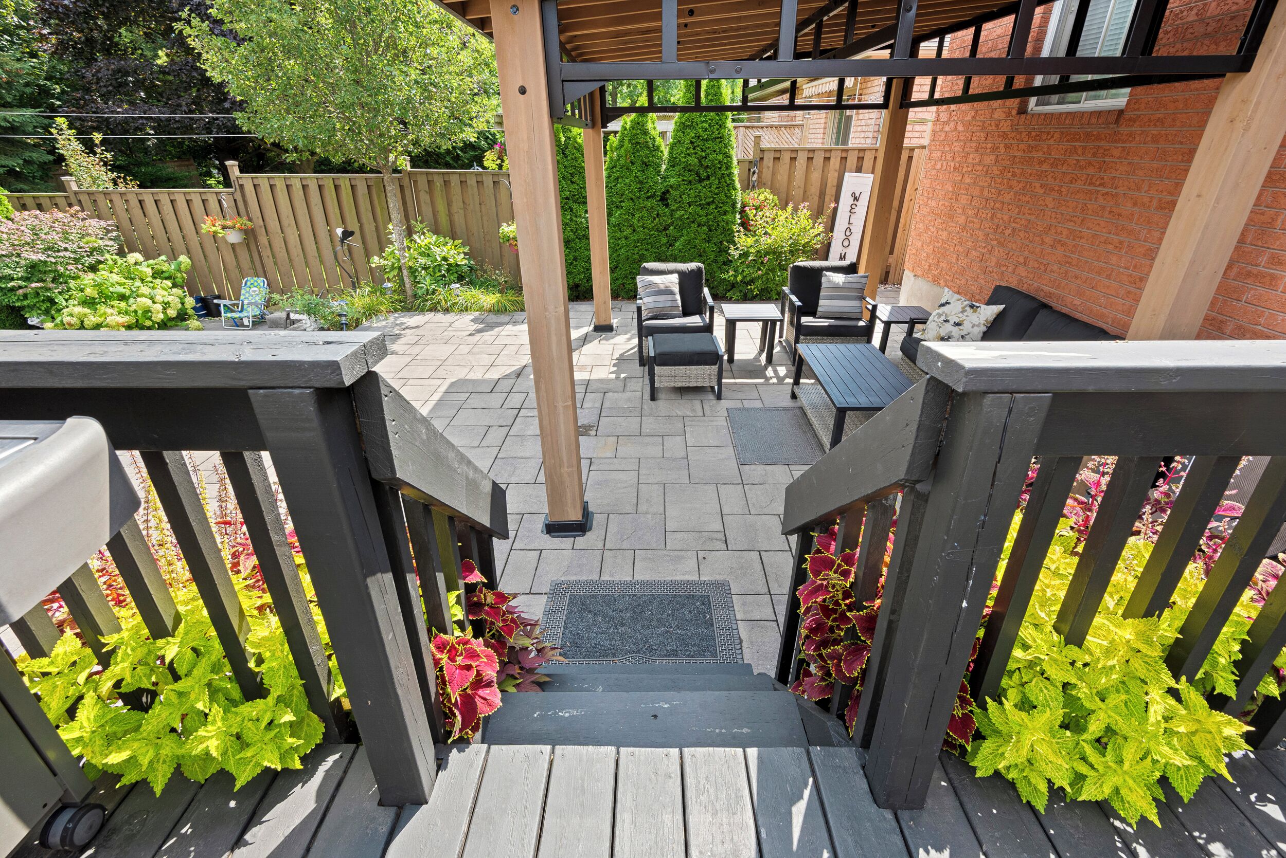 En træterrasse med pergola, udendørs møbler og en murstensvæg.