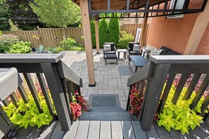 Eine Holzterrasse mit einer Pergola, Gartenmöbeln und einer Ziegelwand.