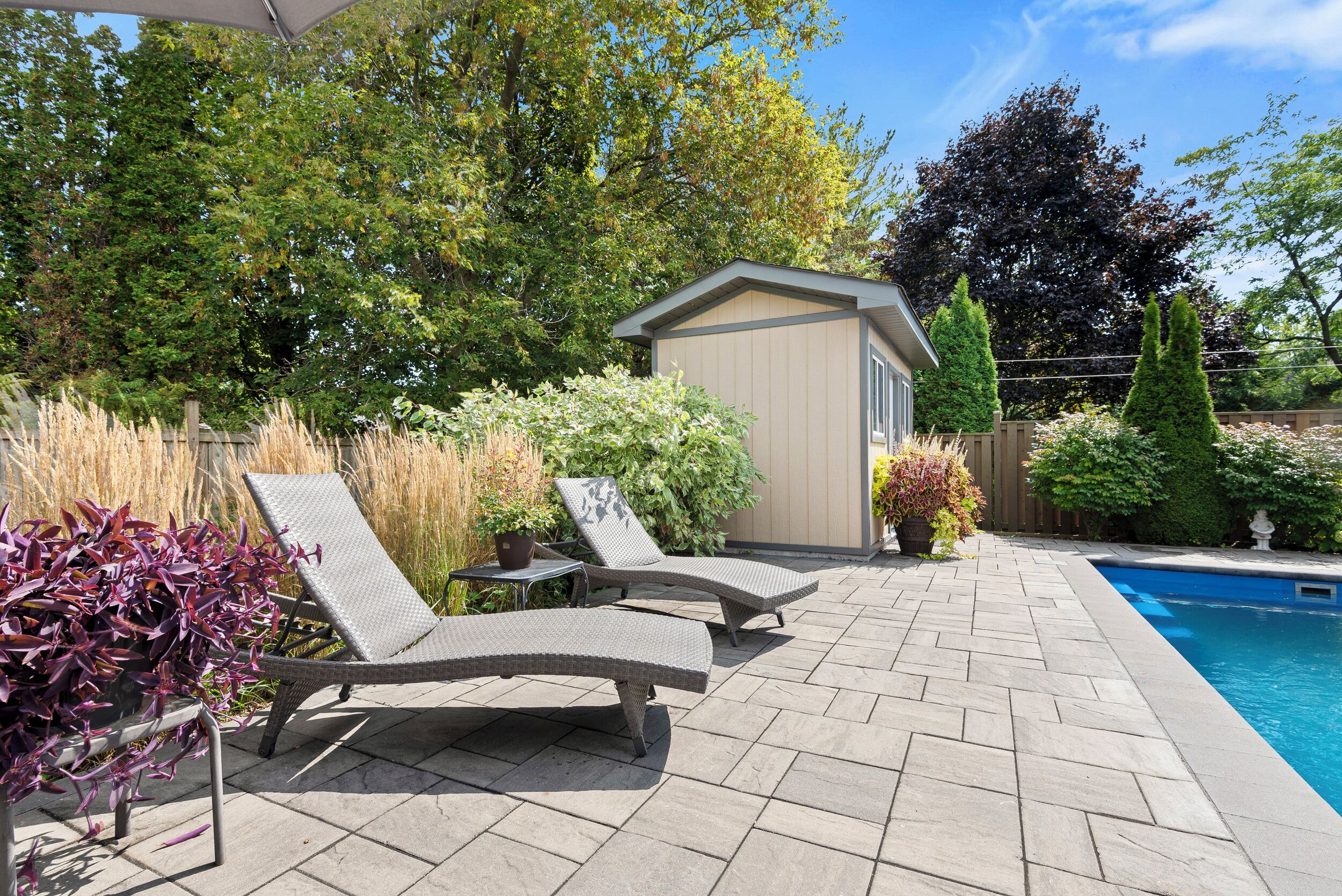 A patio with two lounge chairs, a small shed, and a swimming pool.
