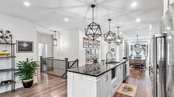 A modern kitchen with a central island, pendant lights, and a staircase leading to another level.