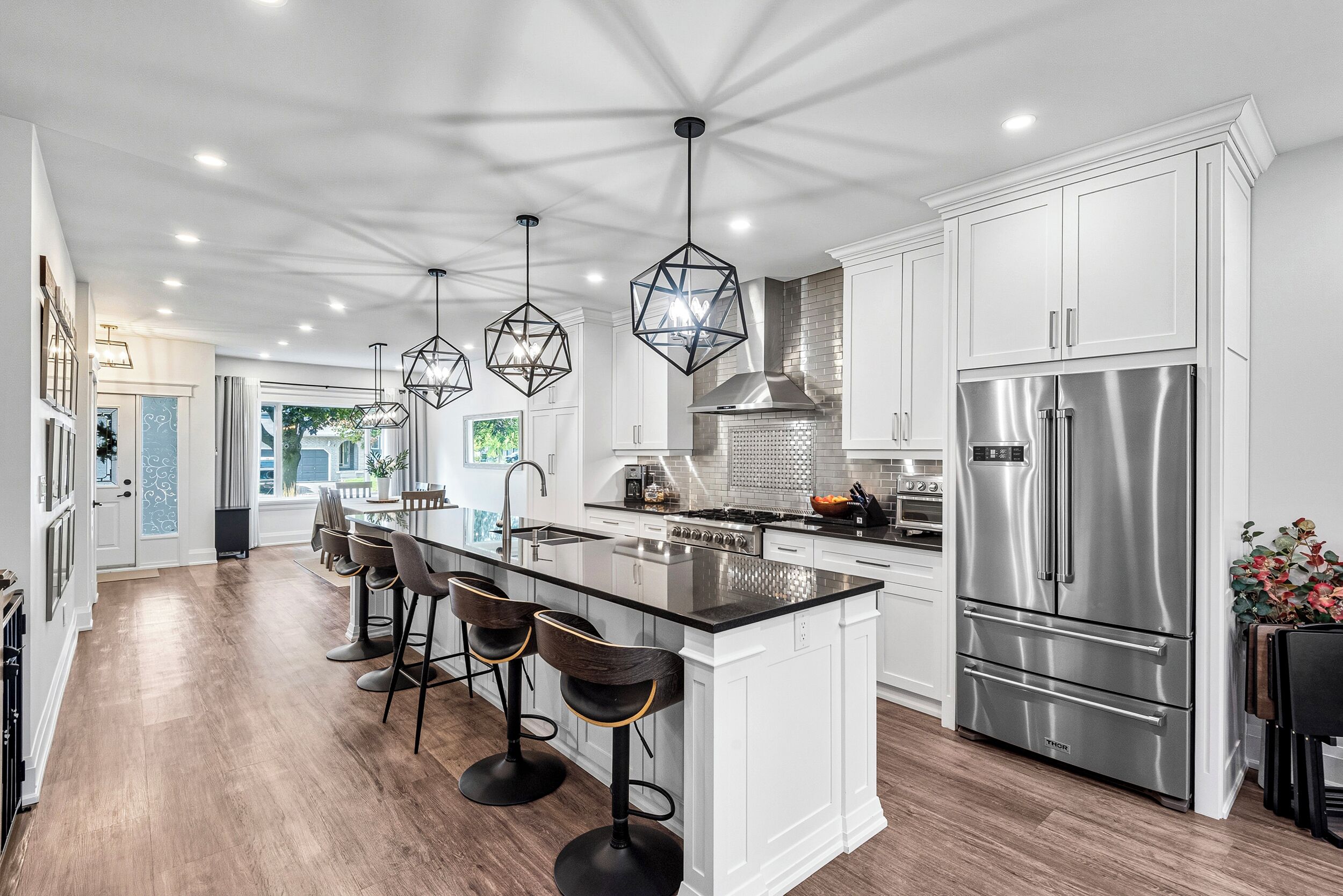 A modern kitchen with a central island, bar stools, stainless steel appliances, and pendant lighting.